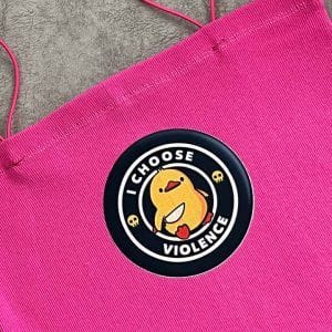 یک تاپ یا کراپ زنانه صورتی با بندهای نازک اسپارگتی. در مرکز سینه تاپ، یک پچ دایره‌ای سیاه با حاشیه سفید و طرح یک جوجه کارتونی زرد رنگ وجود دارد که قلبی قرمز در دست دارد و زیر آن به انگلیسی نوشته شده: "I CHOOSE VIOLENCE" (من خشونت را انتخاب می‌کنم). در اطراف طرح جوجه، جمجمه‌های کوچکی نیز دیده می‌شود. پارچه تاپ به نظر بافت‌دار و راه راه عمودی است و از نمای نزدیک عکاسی شده است .