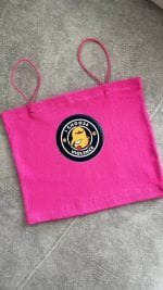 یک تاپ یا کراپ زنانه صورتی با بندهای نازک اسپارگتی. در مرکز سینه تاپ، یک پچ دایره‌ای سیاه با حاشیه سفید و طرح یک جوجه کارتونی زرد رنگ وجود دارد که قلبی قرمز در دست دارد و زیر آن به انگلیسی نوشته شده: "I CHOOSE VIOLENCE" (من خشونت را انتخاب می‌کنم). در اطراف طرح جوجه، جمجمه‌های کوچکی نیز دیده می‌شود. پارچه تاپ به نظر بافت‌دار و راه راه عمودی استو از نمای دورتر عکاسی شده است.