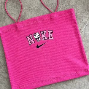 نمای دور یک تاپ یا کراپ زنانه صورتی با بندهای نازک اسپاگتی. در مرکز سینه تاپ، کلمه "NIKE" با حروف بزرگ و به رنگ صورتی با حاشیه مشکی نوشته شده است. به جای حرف "I" در کلمه NIKE، تصویر کارتونی "Hello Kitty" با پاپیون صورتی روی سرش قرار گرفته است. لوگوی معروف نایک (علامت تیک) نیز زیر کلمه NIKE قرار دارد. پارچه تاپ به نظر بافت‌دار و راه راه عمودی است و در پس‌زمینه یک سطح خاکستری دیده می‌شود.